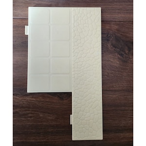 Könnte beinhalten: Eine beige Plastikfliese mit einem Gittermuster auf der linken Seite und einem Steinmuster auf der rechten Seite.