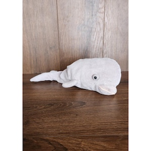 May include: A gray plush toy shaped like a dolphin. The dolphin has a black eye and a pink mouth.