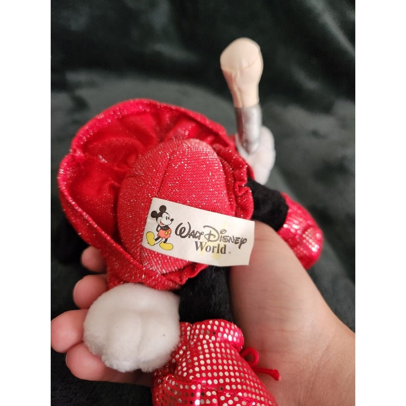 May include: Red plush Mickey Mouse toy wearing a red sequined dress and shoes. The toy has a black face and white gloves. The toy has a tag that says "Walt Disney World".