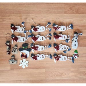 May include: A collection of 20 wooden snowman ornaments with red, white, and black paint. The ornaments are decorated with various patterns and designs, including snowflakes, trees, and stars. Some of the ornaments have a 3D effect, while others are flat. The ornaments are perfect for adding a festive touch to your home during the holiday season.