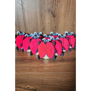May include: A collection of eight plush ladybird toys arranged in a group. Each ladybird features a bright red body with black accents, white eyes, and antennae. The bottom of each plush toy is marked with a yellow number ranging from one to ten.