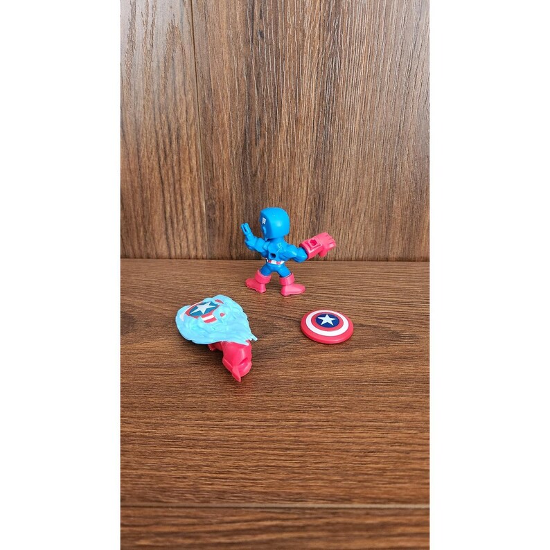 May include: A Captain America action figure with a blue helmet and suit, red gloves and boots, and a shield. The figure is posed with its shield and a separate shield piece and a round shield with a star.