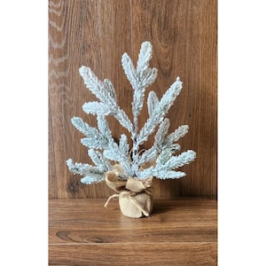 May include: A small, flocked, artificial Christmas tree with a burlap base. The tree is decorated with a burlap bow.