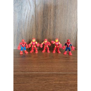 May include: Five superhero action figures, including Spider-Man and Iron Man, are arranged in a row. The figures are primarily red, blue, and yellow, with a cartoonish design. The background is a wooden surface.