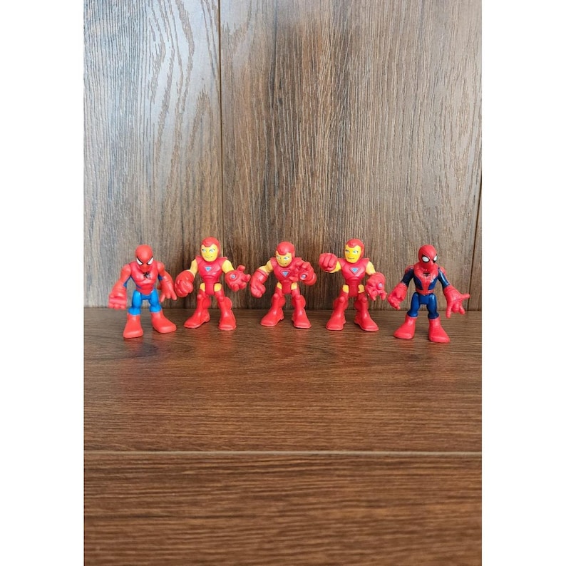 May include: Five superhero action figures, including Spider-Man and Iron Man, are arranged in a row. The figures are primarily red, blue, and yellow, with a cartoonish design. The background is a wooden surface.
