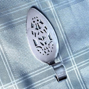 May include: A silver cake server with a decorative, openwork design. The server has a curved handle and a wide, oval-shaped blade. The background is a light blue, textured fabric.