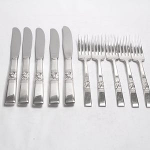 May include: A set of stainless steel cutlery, comprising six butter knives and eight forks. The silverware features a decorative floral pattern on the handles. The knives have a rounded blade, and the forks have four prongs.
