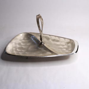 May include: A silver serving tray with a textured surface and a handle. The tray is divided into two sections and has a curved shape. The handle is twisted and rises from the centre of the tray.