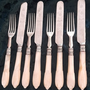 May include: A collection of antique cutlery, comprising forks and knives. The blades and tines are silver, featuring intricate floral patterns. The handles are a pale, creamy hue with a carved design. The set includes four forks and four knives.