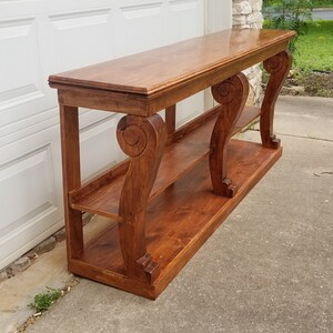 Op de afbeelding: Een houten consoletafel met twee planken en sierlijke, gerolde poten. De tafel is in een rijke bruine kleur gebeitst en heeft een gladde, gepolijste afwerking.