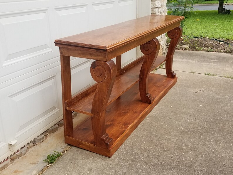 Op de afbeelding: Een houten consoletafel met twee planken en sierlijke, gerolde poten. De tafel is in een rijke bruine kleur gebeitst en heeft een gladde, gepolijste afwerking.