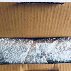 May include: An open cardboard box with bubble wrap inside. The bubble wrap is secured with a rubber band.