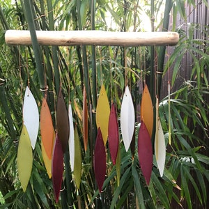 May include: A wind chime made of wood and glass. The glass pieces are shaped like leaves and are in shades of red, orange, yellow, and green. The wind chime is hanging from a branch.