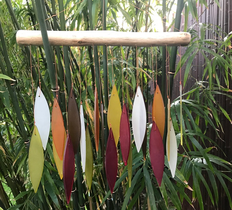 May include: A wind chime made of wood and glass. The glass pieces are shaped like leaves and are in shades of red, orange, yellow, and green. The wind chime is hanging from a branch.