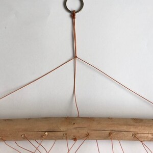 May include: A brown cord is tied to a metal ring and then to a wooden branch. The cord is strung across the branch to create a hanging macrame design.