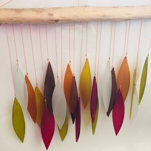 May include: A driftwood wind chime with multiple glass leaves in shades of green, red, brown, and white.