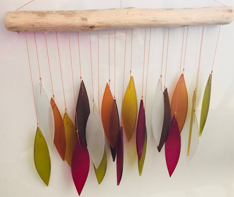 May include: A driftwood wind chime with multiple glass leaves in shades of green, red, brown, and white.