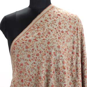 May include: A beige shawl with a delicate floral pattern in shades of orange and red. The shawl is made of soft, lightweight fabric and is perfect for adding a touch of elegance to any outfit.