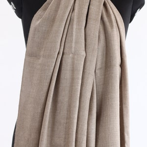 May include: A light brown pashmina scarf draped over a black mannequin. The scarf is made of a soft, woven fabric and has a subtle sheen.