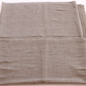May include: A plain, light brown fabric shawl folded in half. The fabric has a subtle texture and a slightly rough feel.