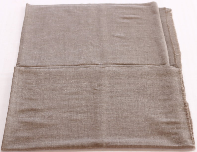 May include: A plain, light brown fabric shawl folded in half. The fabric has a subtle texture and a slightly rough feel.