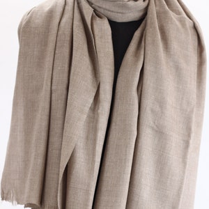 May include: A light brown pashmina scarf made of soft fabric. The scarf is draped over a mannequin and has a fringed edge.