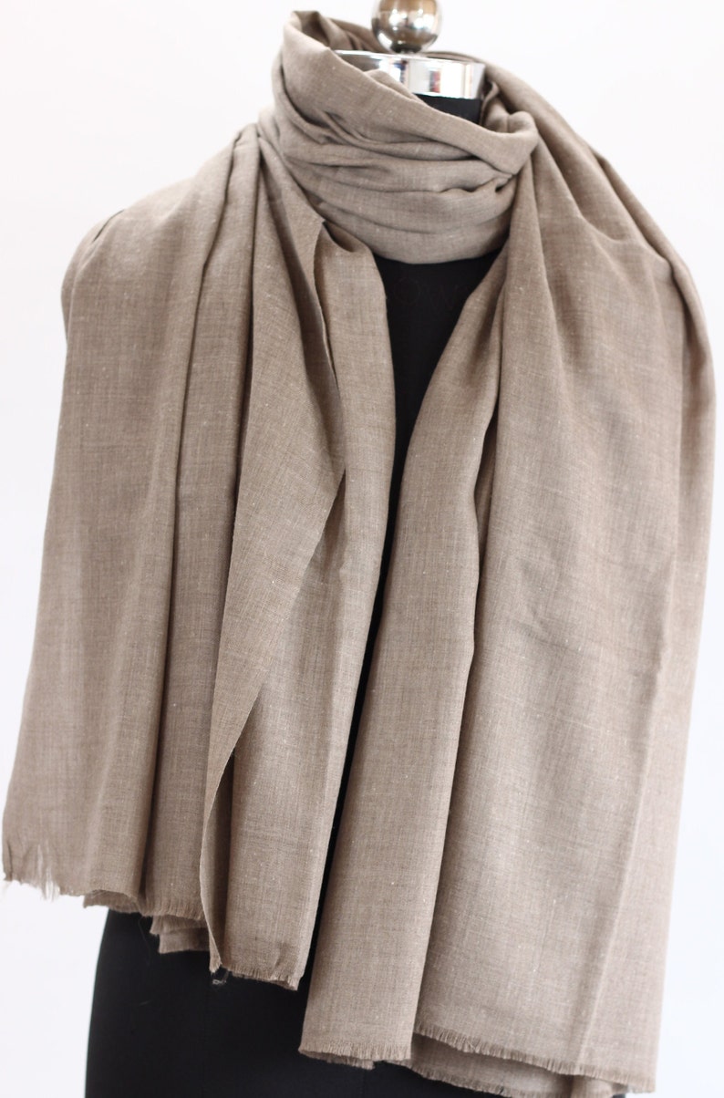 May include: A light brown pashmina scarf made of soft fabric. The scarf is draped over a mannequin and has a fringed edge.