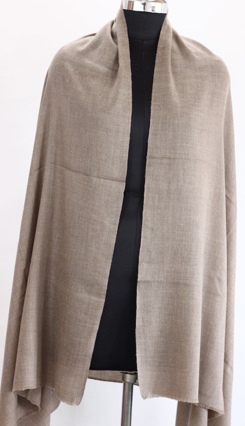 May include: A light brown pashmina shawl made of soft wool. The shawl is draped over a mannequin and has a simple, elegant design.