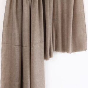 May include: A brown pashmina shawl made of soft, luxurious fabric. The shawl is draped over a wooden dowel and hangs down in a graceful curve.