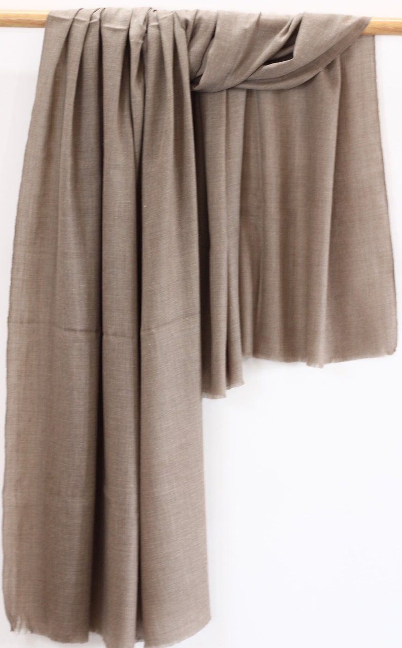 May include: A brown pashmina shawl made of soft, luxurious fabric. The shawl is draped over a wooden dowel and hangs down in a graceful curve.