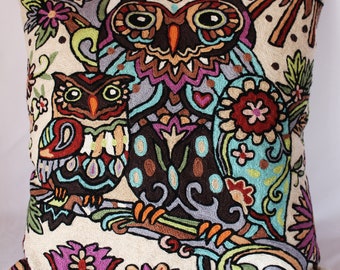 May include: A cream-coloured throw pillow with an embroidered design of two owls with colourful floral accents. The owls are brown, blue, green, and pink.