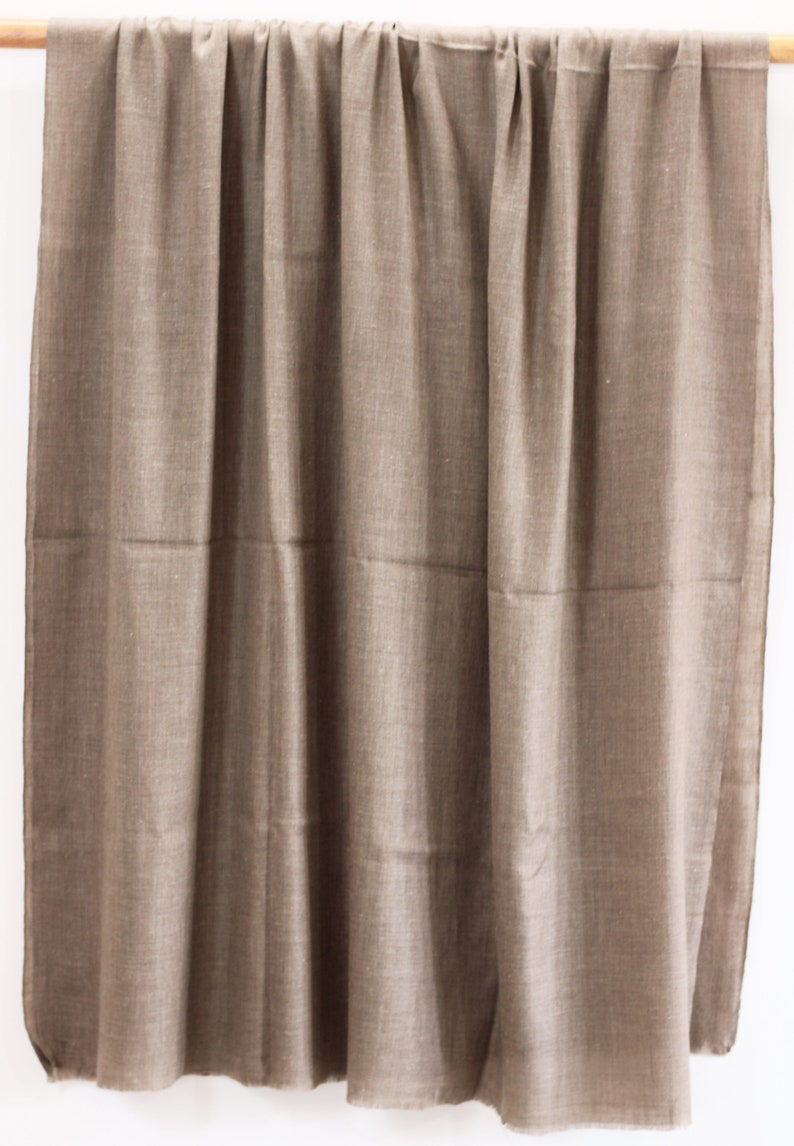 May include: A brown woven shawl hanging on a wooden rod. The shawl is made of a soft, lightweight fabric and has a subtle sheen.