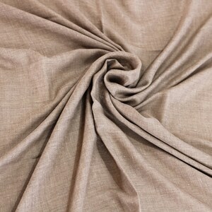 May include: A close-up of a brown fabric with a textured surface. The fabric is folded and draped in a way that creates a swirling pattern.