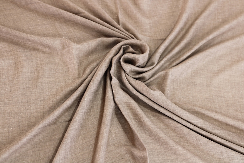 May include: A close-up of a brown fabric with a textured surface. The fabric is folded and draped in a way that creates a swirling pattern.