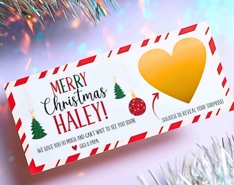 May include: A rectangular Christmas gift card with a red and white striped border. It features the text MERRY CHRISTMAS HALEY!, a green Christmas tree, a red ornament, a gold scratch-off heart, and the text SCRATCH TO REVEAL YOUR SURPRISE!