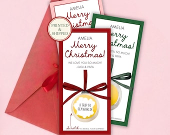 May include: Three rectangular Christmas gift cards with envelopes, featuring the text AMELIA, Merry Christmas!, WE LOVE YOU SO MUCH! -GIGI & PAPA, and A TRIP TO SEAWORLD! inside a scratch-off ornament graphic with a red ribbon and a PRINTED & SHIPPED seal.