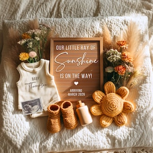 May include: A neutral-toned baby announcement featuring a letter board with the text "OUR LITTLE RAY OF Sunshine IS ON THE WAY! ARRIVING MARCH 2026". The announcement includes a onesie, booties, a bottle, and a crocheted flower.