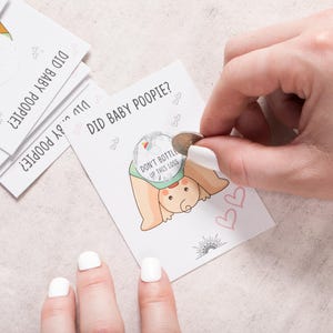 Pode incluir: Um cart&atilde;o de jogo com o texto "Did baby poopy?" e uma ilustra&ccedil;&atilde;o de desenho animado de um beb&ecirc; com uma fralda. O cart&atilde;o tem um adesivo prateado que diz "N&atilde;o engarrafar este lan&ccedil;amento".
