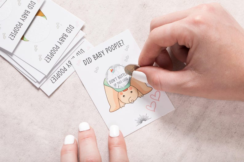 Pode incluir: Um cart&atilde;o de jogo com o texto "Did baby poopy?" e uma ilustra&ccedil;&atilde;o de desenho animado de um beb&ecirc; com uma fralda. O cart&atilde;o tem um adesivo prateado que diz "N&atilde;o engarrafar este lan&ccedil;amento".