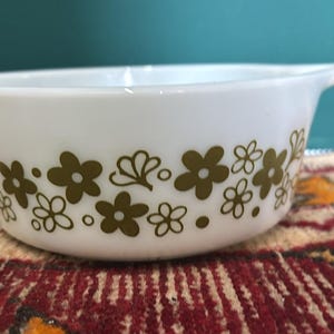 以下が含まれることがあります： 緑色の花柄の白いキャセロール。キャセロールにはハンドルが2つ付いています。