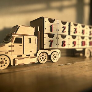 May include: A wooden toy truck with a trailer. The trailer has 10 compartments, each with a number from 1 to 10. The truck is brown and the trailer is beige.