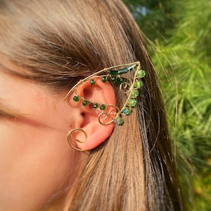 May include: Gold ear cuff with green crystal beads and a wire design resembling a leaf. The cuff is worn on the upper part of the ear.