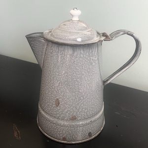 May include: A gray enamel coffee pot with a white knob on the lid. The pot has a speckled pattern and a wide spout.