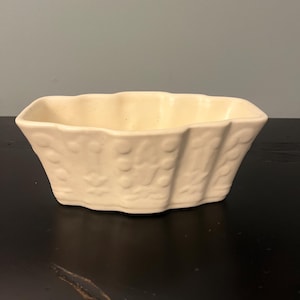 May include: A white ceramic planter with a wavy, scalloped edge and a textured design. The planter is empty.