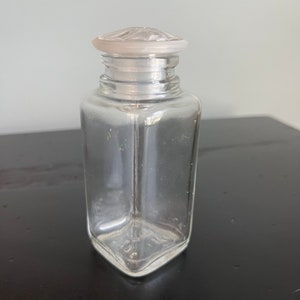 May include: A clear glass bottle with a frosted glass lid. The bottle has a square shape and is empty.