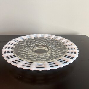 May include: A white milk glass cake plate with a woven pattern and a scalloped edge.