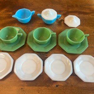 May include: A vintage children's tea set with three green cups and saucers, three white saucers, a blue teapot, and a white sugar bowl with lid.