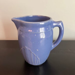 May include: A light blue ceramic pitcher with a white design. The pitcher has a rounded body and a handle.