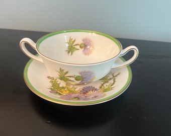Peut inclure: Un bol à soupe en porcelaine blanche avec un bord vert et un motif floral de chardons violets. Le bol est sur une soucoupe assortie.