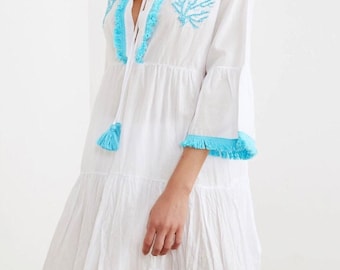 May include: White cotton dress with blue embroidered coral designs and blue tassel ties. The dress has a V-neckline and a tiered skirt.